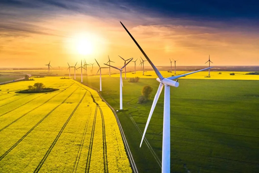 Windkraftwerke auf Feldern produzieren Strom aus Erneuerbaren Energien. Im Hintergrund steht die Sonne tief am Himmel