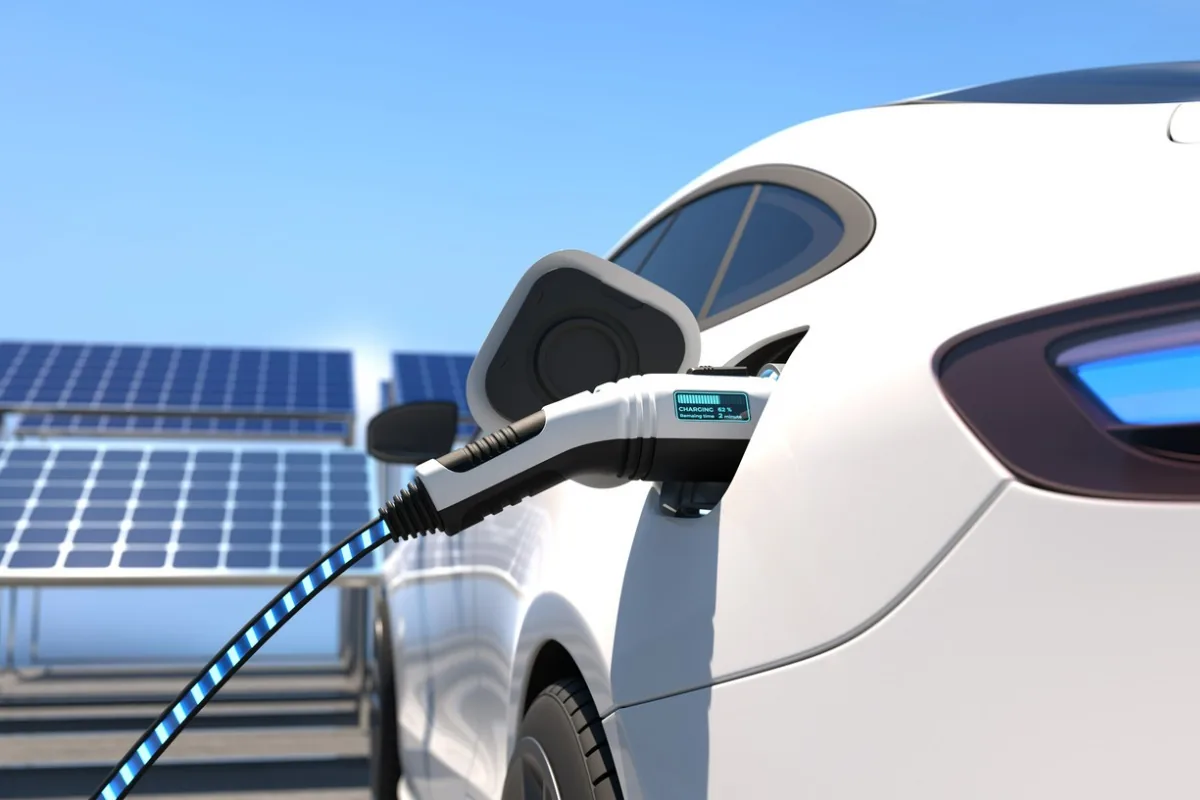 Ein E-Auto wird geladen. Im Hintergrund sind Solaranlagen zu sehen. 