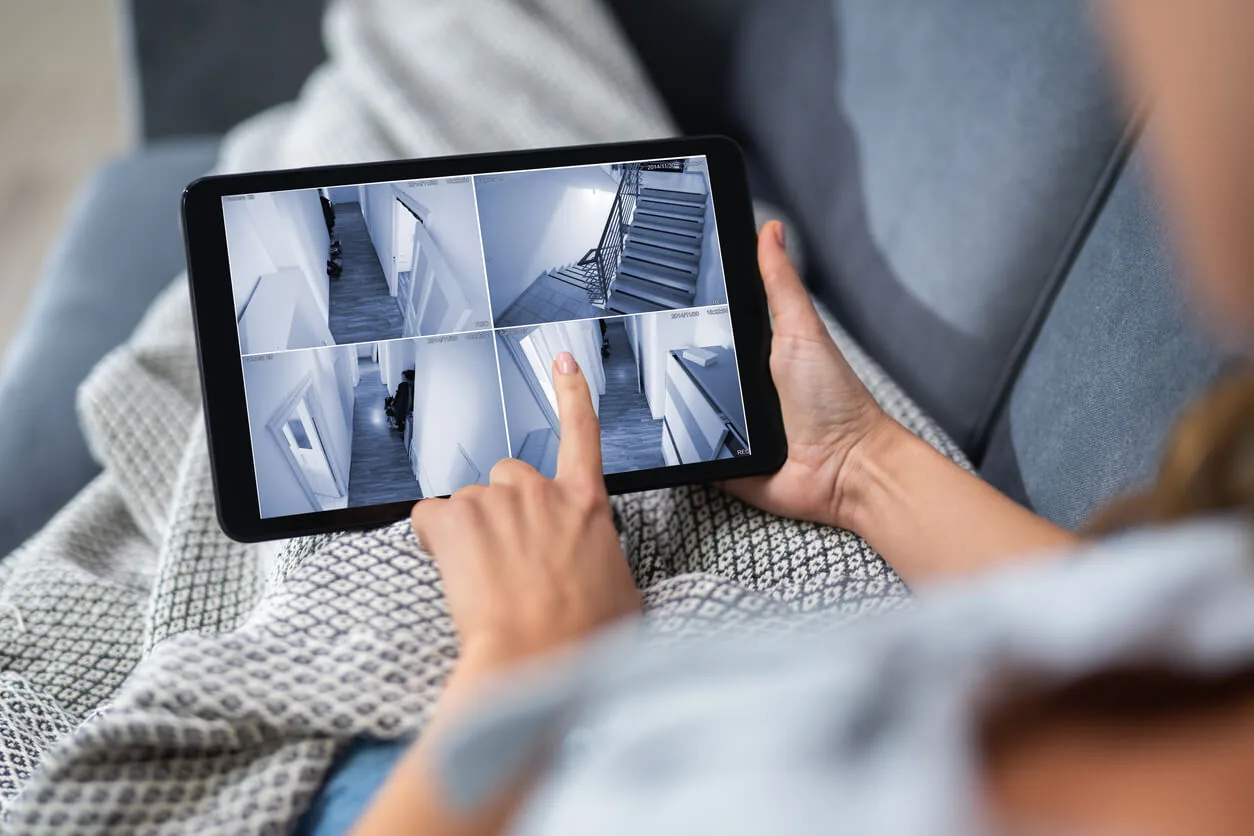 Sorgloser Urlaub: Person schaut auf einem Tablet Kameraaufnahmen von Ihrem Zuhause an.