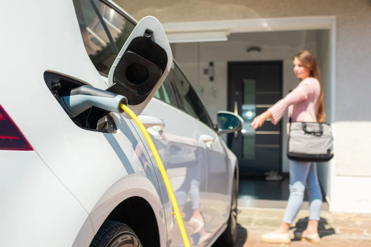 Ein Elektroauto lädt über eine Wallbox in der Einfahrt eines Wohnhauses.